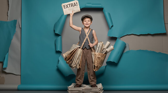 Young boy newsboy holding newspaper aloft through torn blue paper background, wearing vintage clothing and satchel bags. Retro concept, advertising, journalism, childhood nostalgia.