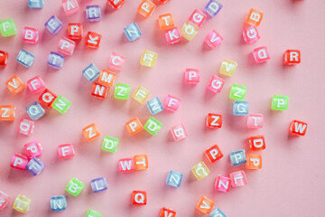 Colorful letter alphabet bead cubes scattered randomly on pink background  © Afi