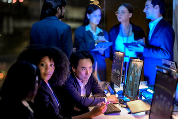 Cross-functional team tracking system performance overnight in a low-light innovation lab, working...