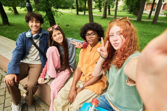 Portrait of diverse multiethnic teenagers taking selfie outdoors in park while showing peace signs. Visual asset suitable for youth lifestyle marketing and mobile app campaigns