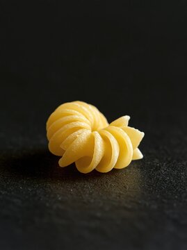 Single piece of raw rotini pasta isolated on a dark textured background with copy space