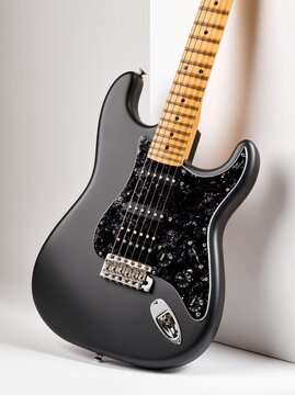Matte black electric guitar leaning against a white wall with copy space for musical event promotion