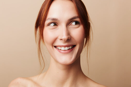 Young redhead woman with bare shoulders smiling broadly and glancing curiously to the side. Happy playful expression concept for beauty and advertising layouts.