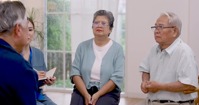 Senior Asian man and woman discuss health concerns with Asian nurse, who listens and records notes during rehabilitation consultation about wellness support, recovery needs and daily care in center.