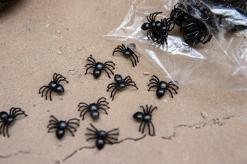 Fototapeta premium Small black artificial spiders scattered on a textured surface as spooky Halloween decorations. Creepy seasonal props for Halloween parties, crafts and festive displays.