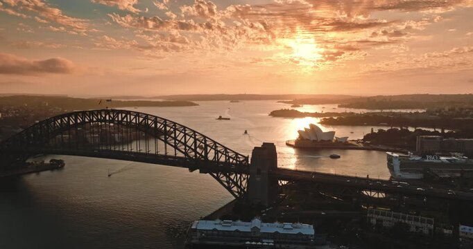 Sydney Harbour skyline during a vibrant orange sunrise. Iconic Sydney Harbour Bridge and Opera House, boats navigating the calm bay water. Australia famous landmarks. Aerial view drone flight panorama