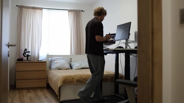 Young entrepreneur checks his planner while walking on a treadmill organizing daily goals and computer tasks to combine time management with movement during a busy workday