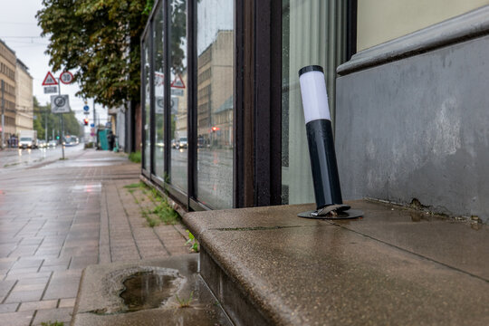 Bent Outdoor Lamp Beside a Rainy Urban Sidewalk