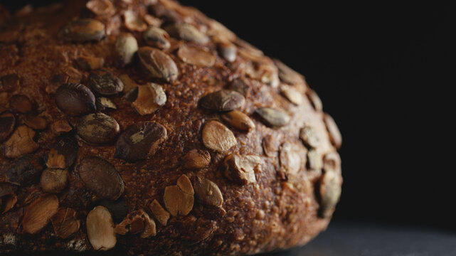 Close-up of artisan whole wheat sourdough bread topped with pumpkin seeds on a dark background. Freshly baked organic loaf with crispy crust for commercial bakery promotions and healthy food concept.