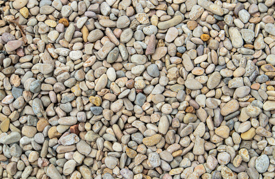 Top down view of rounded gravel and river pebbles in beige, tan, and grey tones on a dry surface