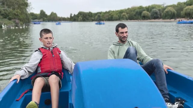 Father and son riding pedal boat together on park lake