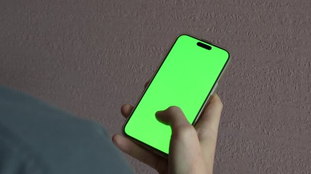 4K footage of man holding smartphone with green screen, scrolling and swiping display close up
