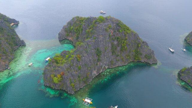 Aerial view of a rugged limestone island surrounded by vivid turquoise shallows and darker open water in Coron Palawan