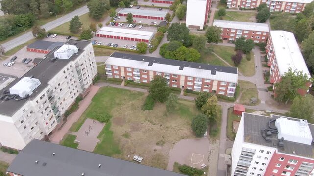 Elevated view of apartments around a patchy lawn with paths, playground, parking and red-gabled garages.