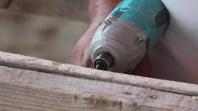 Cordless drill bores pilot hole into structural pine timber within a dusty construction site. Static close up shot.