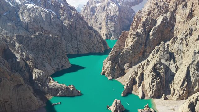 Aerial high-angle view over turquoise emerald waters of alpine Lake Kel-Suu surrounded by sheer limestone cliffs, Kyrgyzstan