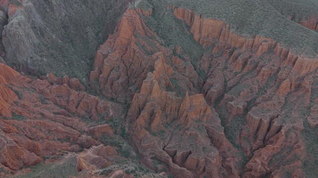 Aerial high-angle overview of rugged red sandstone formations and deep eroded ravines in Kok-Moynok Canyon, Kyrgyzstan