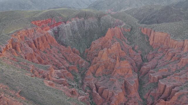 Aerial high-angle overview of rugged red sandstone formations and deep eroded ravines in Kok-Moynok Canyon, Kyrgyzstan
