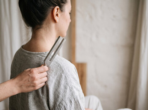Practitioner applying vibrating tuning fork to woman neck during sound healing therapy