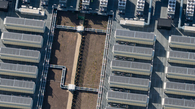 Aerial view of an industrial data center facility featuring rows of cooling units and complex piping systems in Dietzenbach, Hessen, Germany.