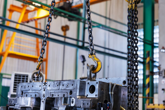 Industrial Crane Lifting a Metal Mold with Chains and Hooks in a Factory