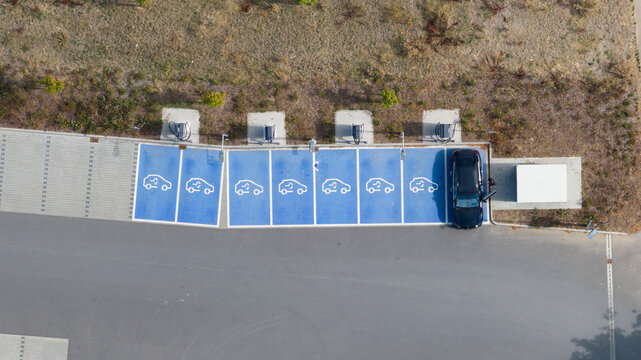 Aerial view of an electric vehicle charging station with blue marked parking spaces and charging units in Liederbach am Taunus, Hessen, Germany.