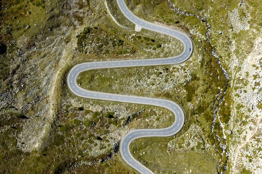 Aerial view of the winding road of Julier Pass with sharp curves, rocky alpine terrain, and green mountain slopes in Surses, Grisons, Switzerland.