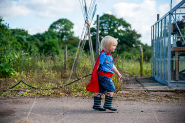 Child in superhero costume walks outdoors near a greenhouse. © Rawpixel.com