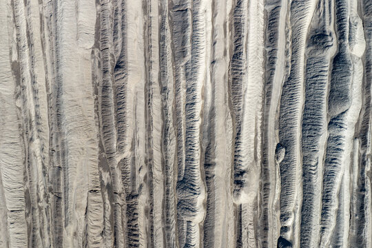 Aerial view of the textured, eroded landscape of the Tagebau Welzow-Sud brown coal open-pit mine, showing deep vertical gullies and sediment layers in Spremberg, Brandenburg, Germany.