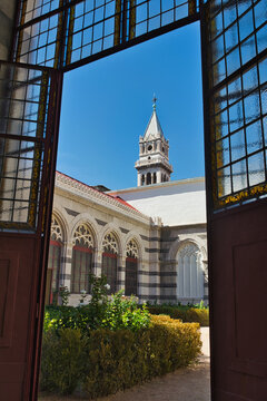 The bell tower of Nuestra Se&ntilde;ora de Atocha School rises above the entrance courtyard of Madrid&rsquo;s Pantheon of Illustrious Men, framed by the dark geometric structure of the gate.