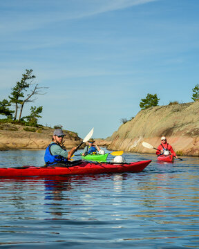 Sea kayaker in a red kayak turns toward camera as paddlers follow through a granite channel with copy space on Georgian Bay, Ontario, Canada