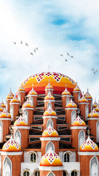 Aerial view of Masjid Kubah 99 Asmaul Husna with its distinctive colorful domes under a bright sky with birds in Kecamatan Mariso, Sulawesi Selatan, Indonesia.