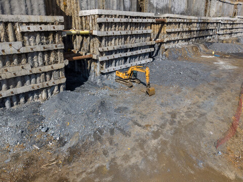 Aerial view of a yellow excavator working at a large construction site with reinforced concrete retaining walls and exposed earth in Istanbul, Istanbul, Turkiye.