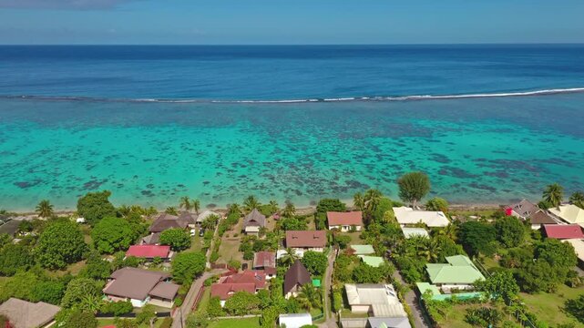Moorea island residential coastline featuring houses and bungalows, vibrant turquoise lagoon, barrier reef and deep blue Pacific Ocean under clear sky. French Polynesia aerial view drone shot panorama