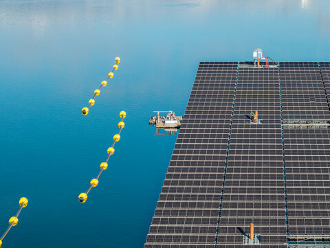 Aerial view of the floating solar farm at Cottbuser Ostsee with workers performing repairs on the panels surrounded by yellow safety buoys on the water in Cottbus, Brandenburg, Germany.