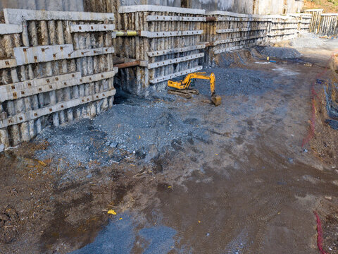 Aerial view of a yellow excavator working at a construction site with concrete retaining walls and excavated earth in Istanbul, Istanbul, Turkiye.