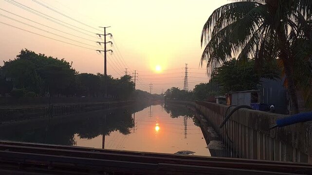 Sunrise over Mookervaart Canal with power grid in West Jakarta