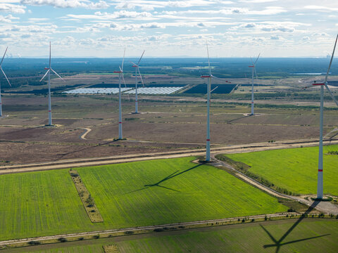 Aerial view of Windpark Forst Briesnig II featuring wind turbines on recultivated land of a former open-pit mine with green fields and solar panels in the distance in Forst, Brandenburg, Germany.