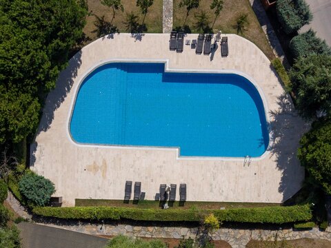 Aerial view of a blue swimming pool surrounded by a stone deck with lounge chairs and lush green hedges in Istanbul, Istanbul, Turkiye.