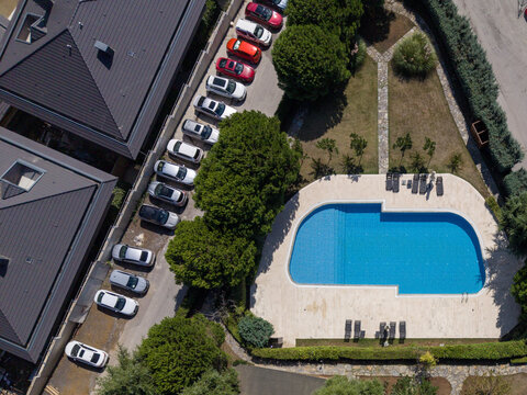 Aerial view of a swimming pool surrounded by a stone deck, lush green trees, and a row of parked cars in a residential area in Istanbul, Istanbul, Turkiye.