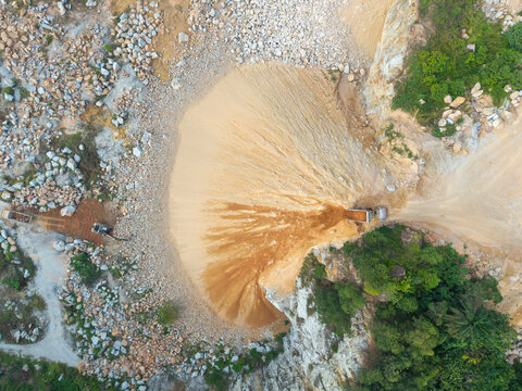 Aerial view of a mining site with heavy machinery extracting sand and soil from rocky terrain surrounded by lush vegetation in Bukit Tambun, Penang, Malaysia.