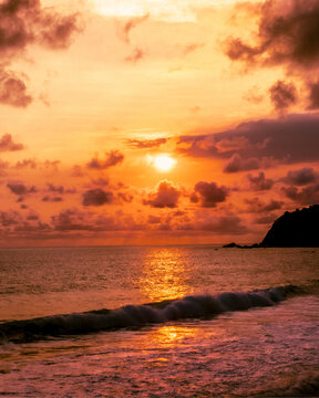 Aerial view of Modangan Beach at sunset with golden light reflecting on the ocean waves and dramatic clouds over the coastline, Donomulyo, East Java, Indonesia.