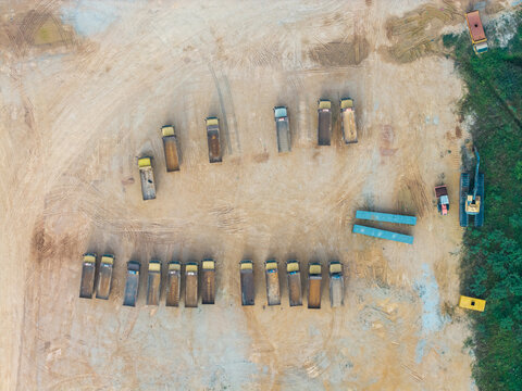 Aerial view of a construction area with rows of parked dump trucks and an excavator on dirt ground in Bukit Tambun, Penang, Malaysia.