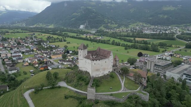 Aerial view of Gutenberg Castle perched on a hill overlooking the town of Balzers with green fields and mountains in the background, Liechtenstein.