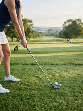 Female golfer holding club preparing to hit golf ball on green grass course background POV view
