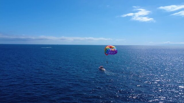 Vista con dron de un barco remolcando un paraca&iacute;das de colores sobre el oc&eacute;ano en un d&iacute;a soleado frente a Tenerife, Islas Canarias, Espa&ntilde;a
