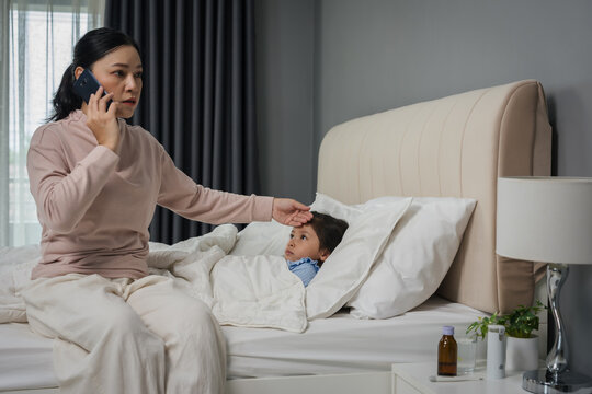 mother talking on smartphone while taking care of sick preschool child girl in bed