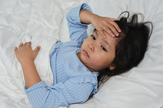 sick preschoool child girl touching her forehead with fever headache in bed