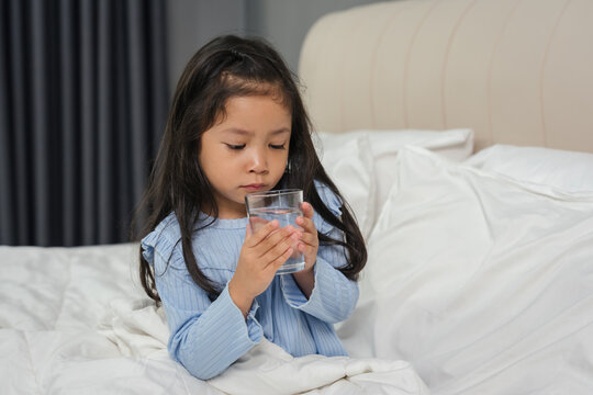 sick preschoool child girl drinking water from glass in bed