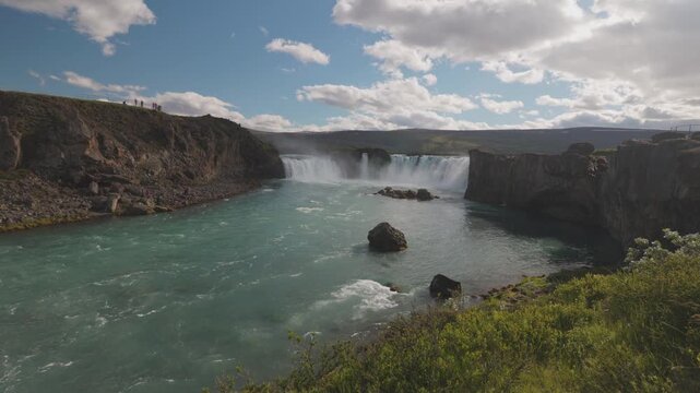 A wide shot of the majestic Godafoss waterfall in Iceland, showing the turquoise river and rocky cliffs under a bright sky. Suitable for travel documentaries and environmental content.